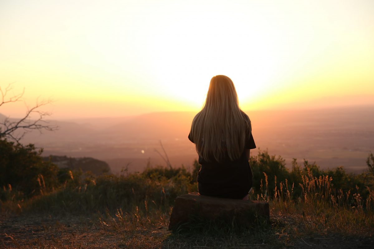 Silhouette of a grieving woman sitting on mountain in sunset view